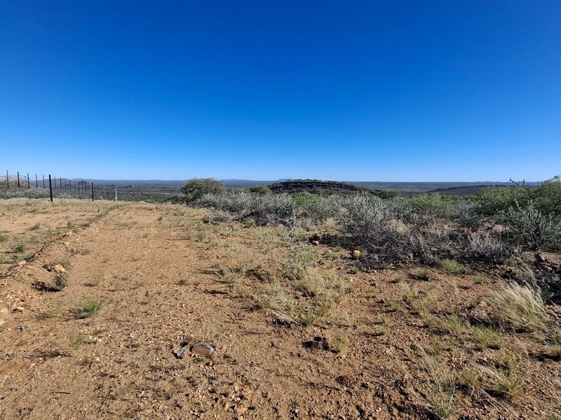 Expansive landscape view overlooking the farm property with natural vegetation and perimeter fencing under a clear blue sky.