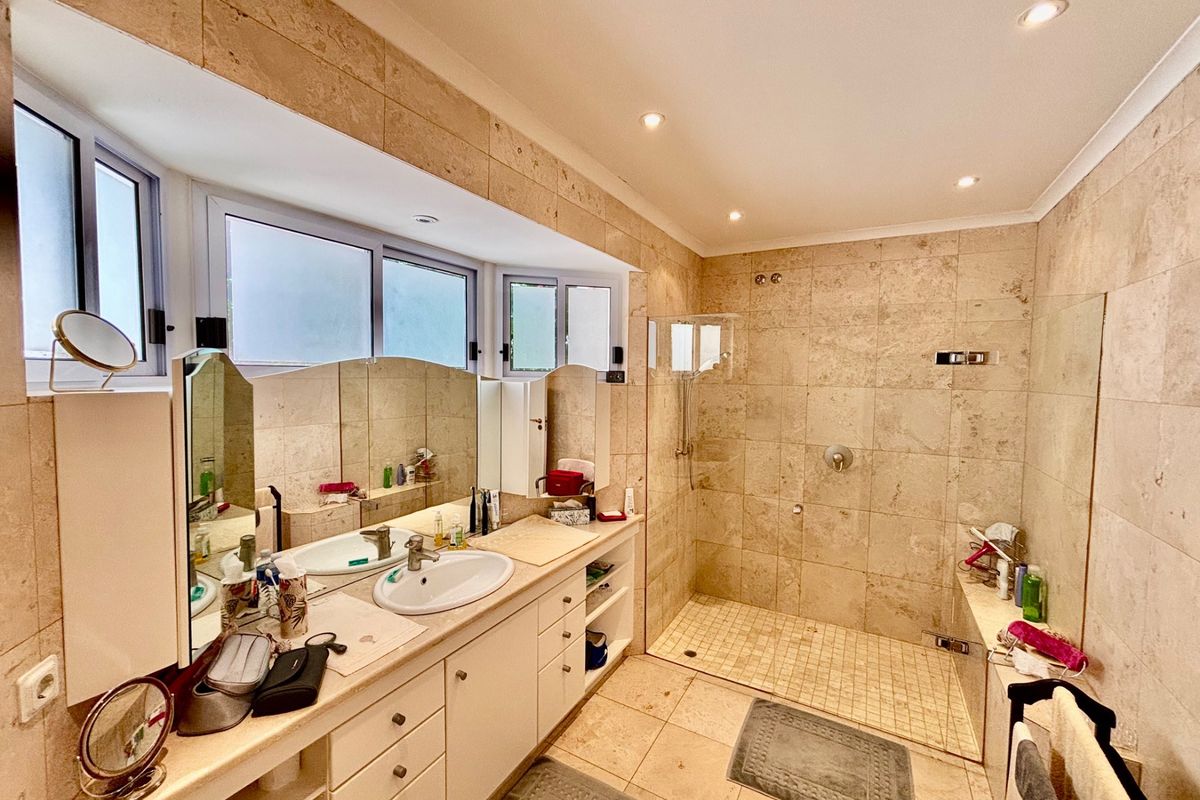 A spacious bathroom featuring floor-to-ceiling travertine tiling, a large walk-in shower with a glass screen, and a vanity with dual basins.