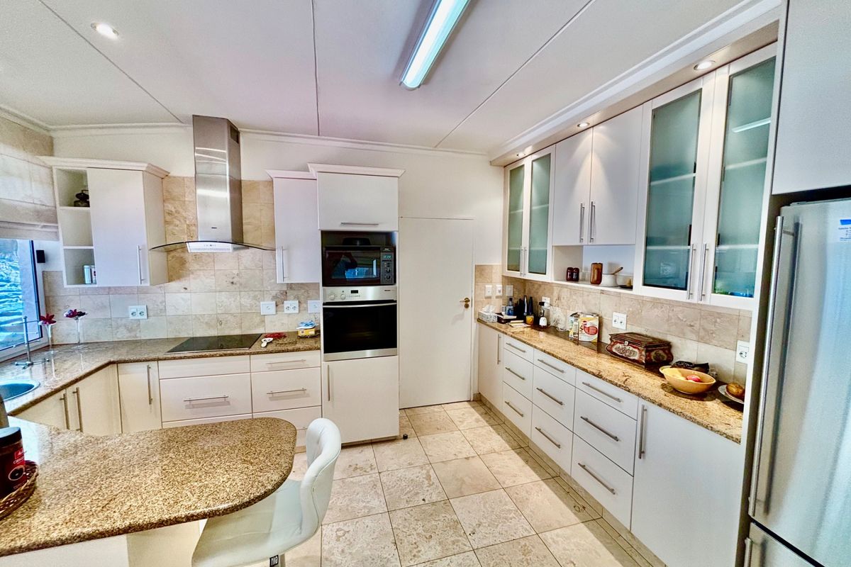 A well-appointed kitchen featuring granite countertops, built-in oven, extractor fan, and ample cabinetry with glass-fronted display units.