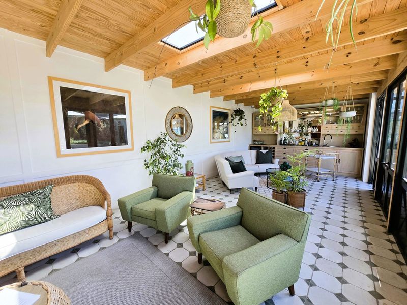 Bright open-plan living area featuring exposed timber beam ceilings, skylights, patterned floor tiles, and a built-in bar area with integrated sink.