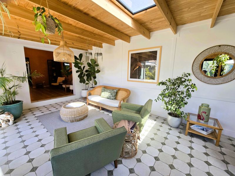 A bright, covered patio area featuring an exposed timber beam ceiling, a skylight, and decorative patterned floor tiles, creating a welcoming indoor-outdoor living space.