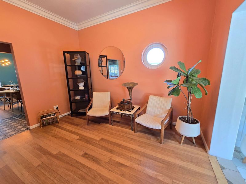 A cozy living area featuring warm-toned walls, polished hardwood flooring, decorative crown molding, and a unique circular porthole window.
