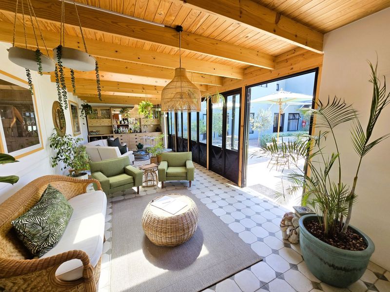 A bright, covered patio area featuring exposed timber beams, patterned tile flooring, and large glass folding doors that open to an outdoor courtyard.