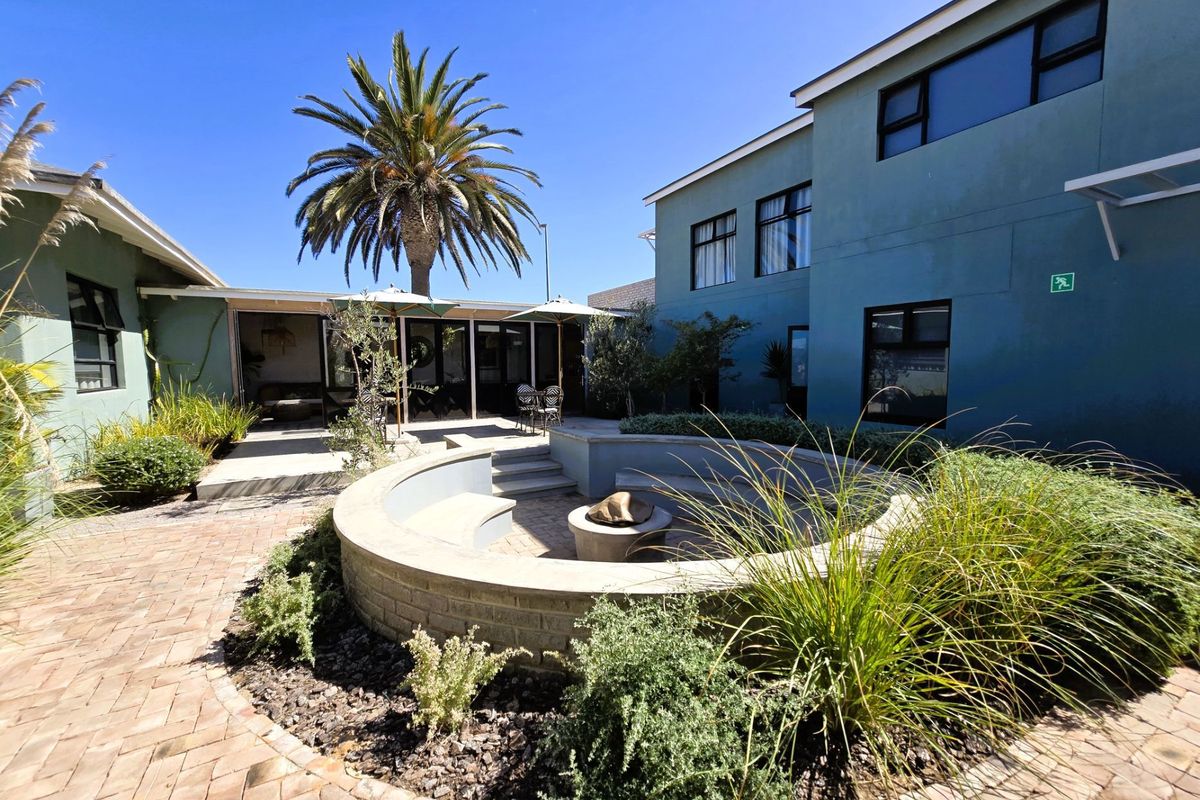 A well-maintained rear courtyard featuring a sunken fire pit with built-in seating, surrounded by landscaped gardens and paved walkways.