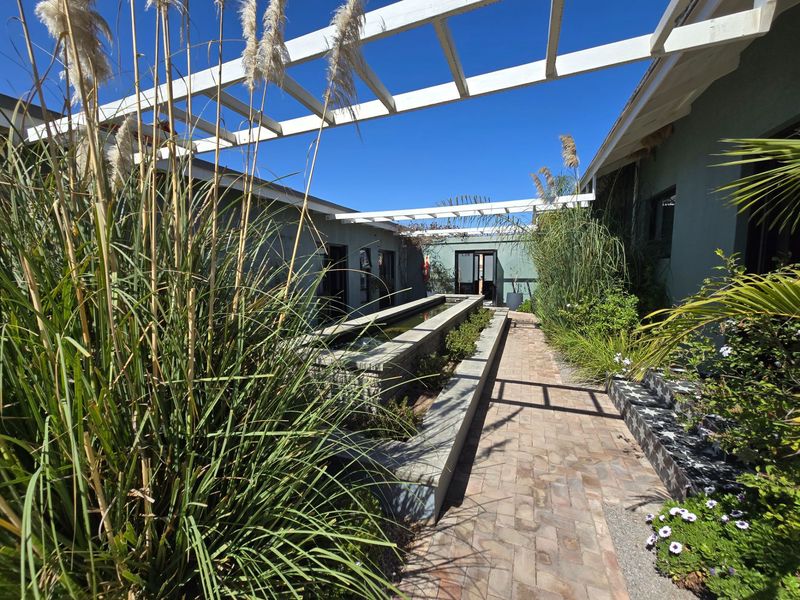 A serene outdoor courtyard featuring a linear water feature, brick paving, and a white timber pergola structure connecting the guest house wings.