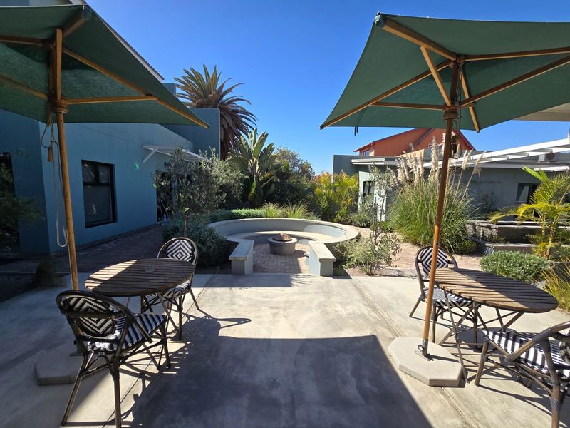 A well-maintained outdoor patio area featuring a built-in circular seating arrangement with a central fire pit, surrounded by landscaped garden beds.