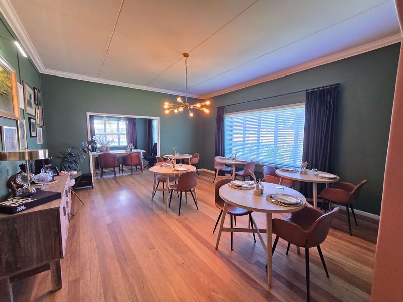 Spacious dining area featuring polished hardwood flooring, elegant green wall finishes, and a modern chandelier, providing a warm and inviting atmosphere for guests.