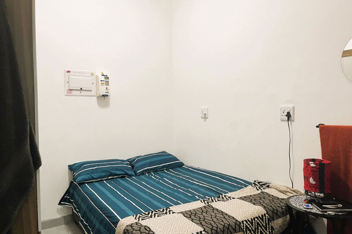 A compact bedroom featuring tiled flooring, built-in electrical distribution board, and wall-mounted power outlets.