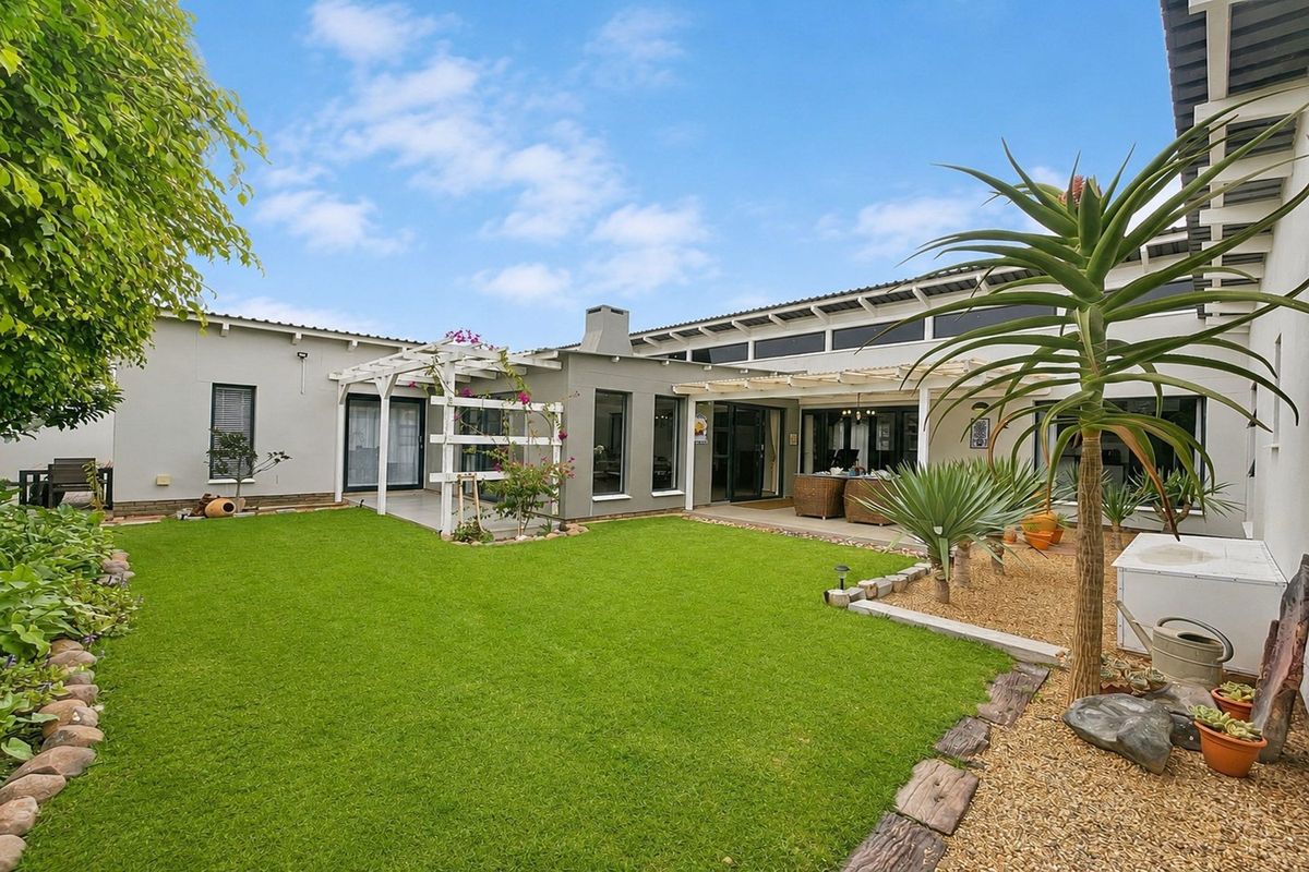 A well-maintained rear garden featuring a lush lawn, landscaped beds, and a covered patio area with a pergola, perfect for outdoor entertaining.