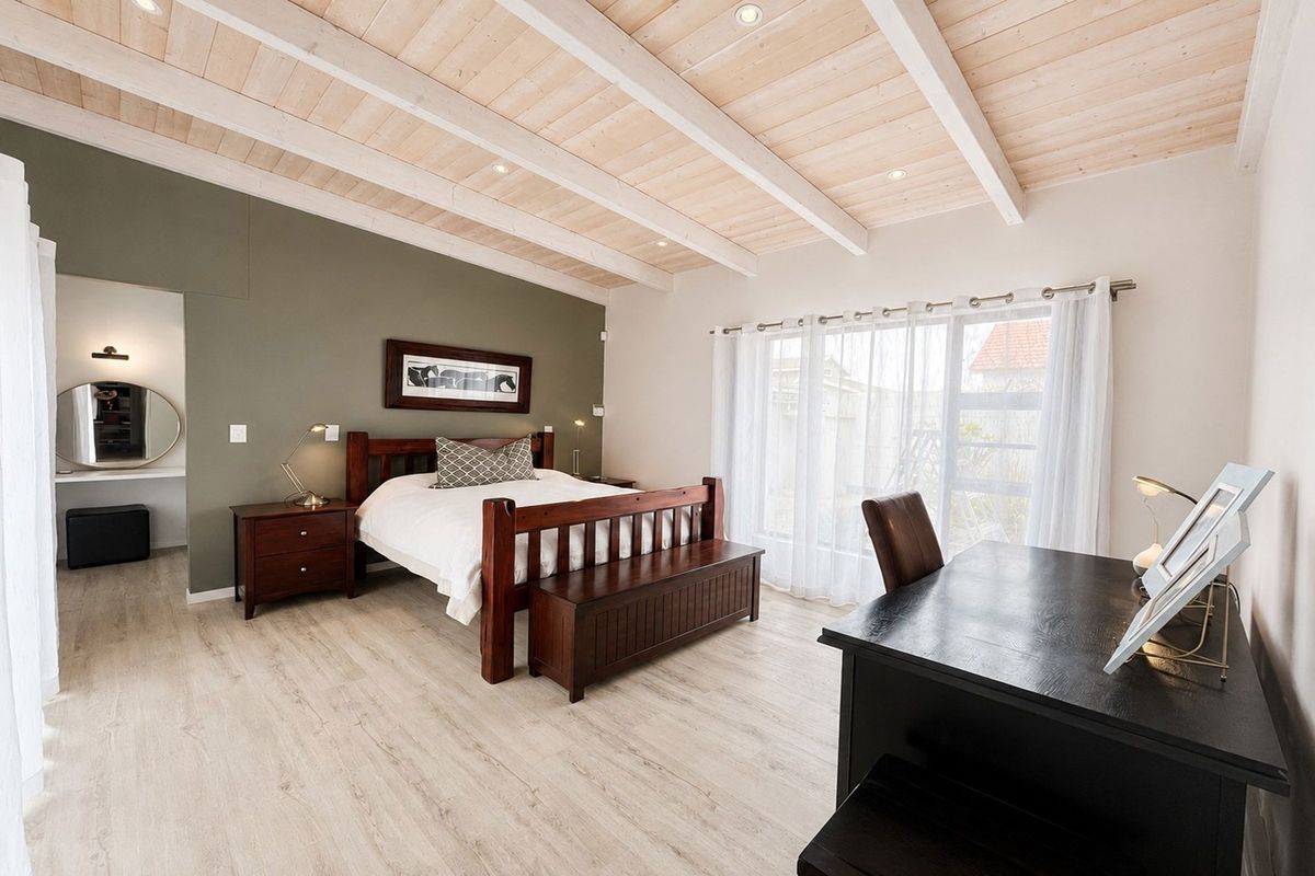 Spacious bedroom featuring a light wood exposed beam ceiling, recessed lighting, laminate flooring, and a sliding glass door providing natural light.