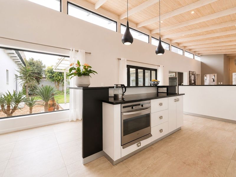 Modern open-plan kitchen featuring a central island with built-in oven, stone countertops, and high exposed timber beam ceilings with clerestory windows.
