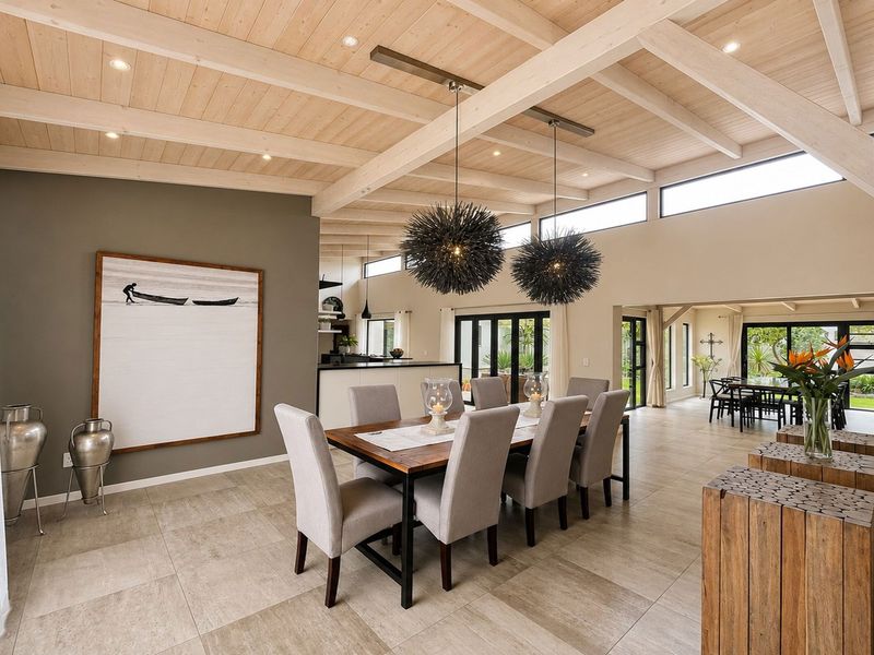 Spacious open-plan living and dining area featuring high exposed timber beam ceilings, large format floor tiles, and seamless access to the outdoor patio.