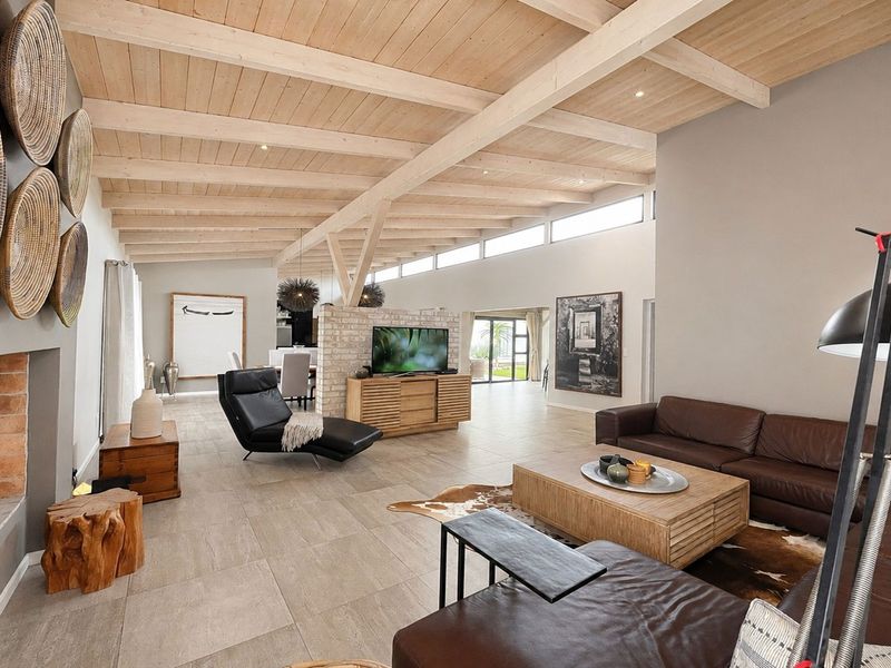 Spacious open-plan living area featuring high exposed timber beam ceilings, tiled flooring, a brick feature wall, and abundant natural light from clerestory windows.