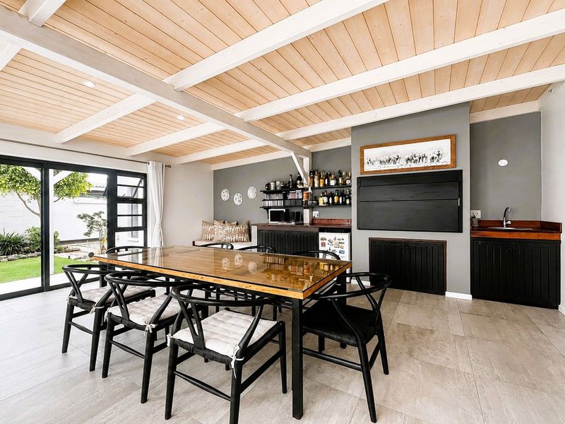 Spacious dining area featuring an exposed timber beam ceiling, built-in bar with sink, and large sliding glass doors opening to the garden.