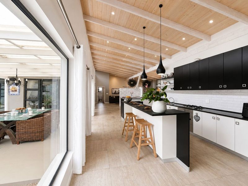 Modern open-plan kitchen featuring sleek cabinetry, a central island, and exposed timber beam ceilings, seamlessly connecting to an adjacent covered patio area.
