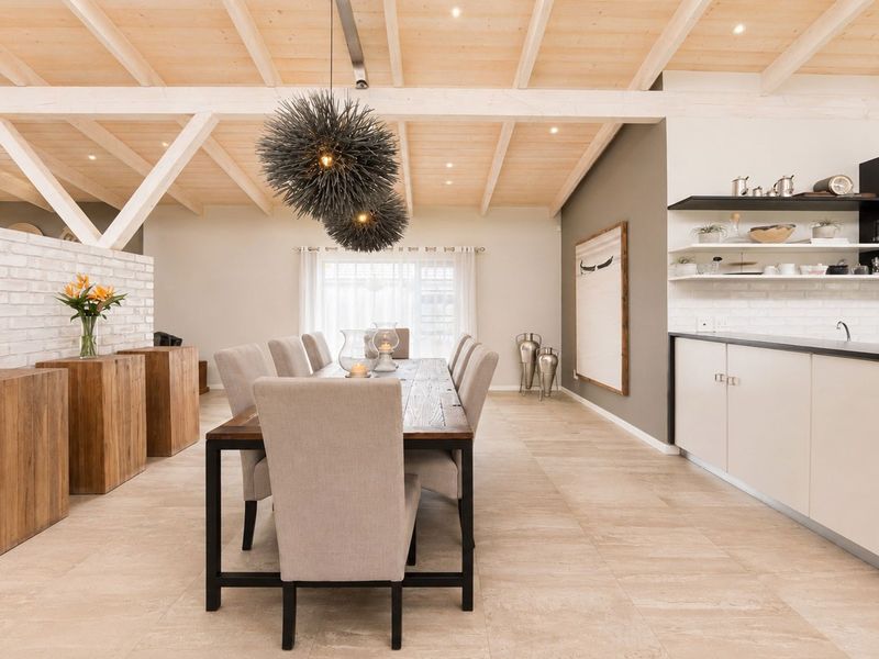 Spacious open-plan dining area featuring a high exposed timber beam ceiling, white brick accents, modern cabinetry, and neutral tiled flooring.