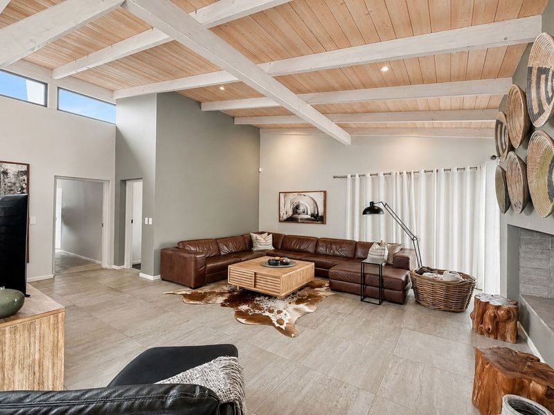 Spacious living room featuring high vaulted ceilings with exposed timber beams, large format floor tiles, and a modern built-in fireplace.