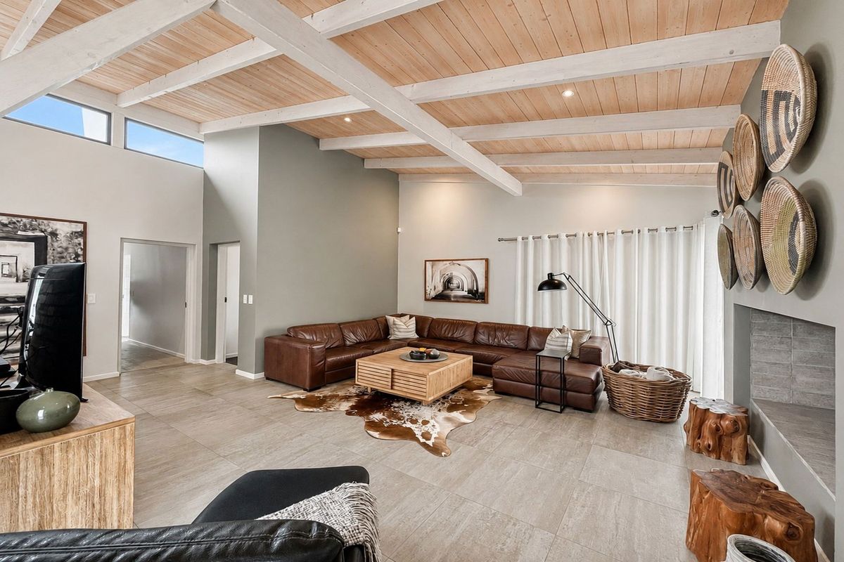 Spacious living room featuring high vaulted ceilings with exposed timber beams, large format floor tiles, and a modern built-in fireplace.