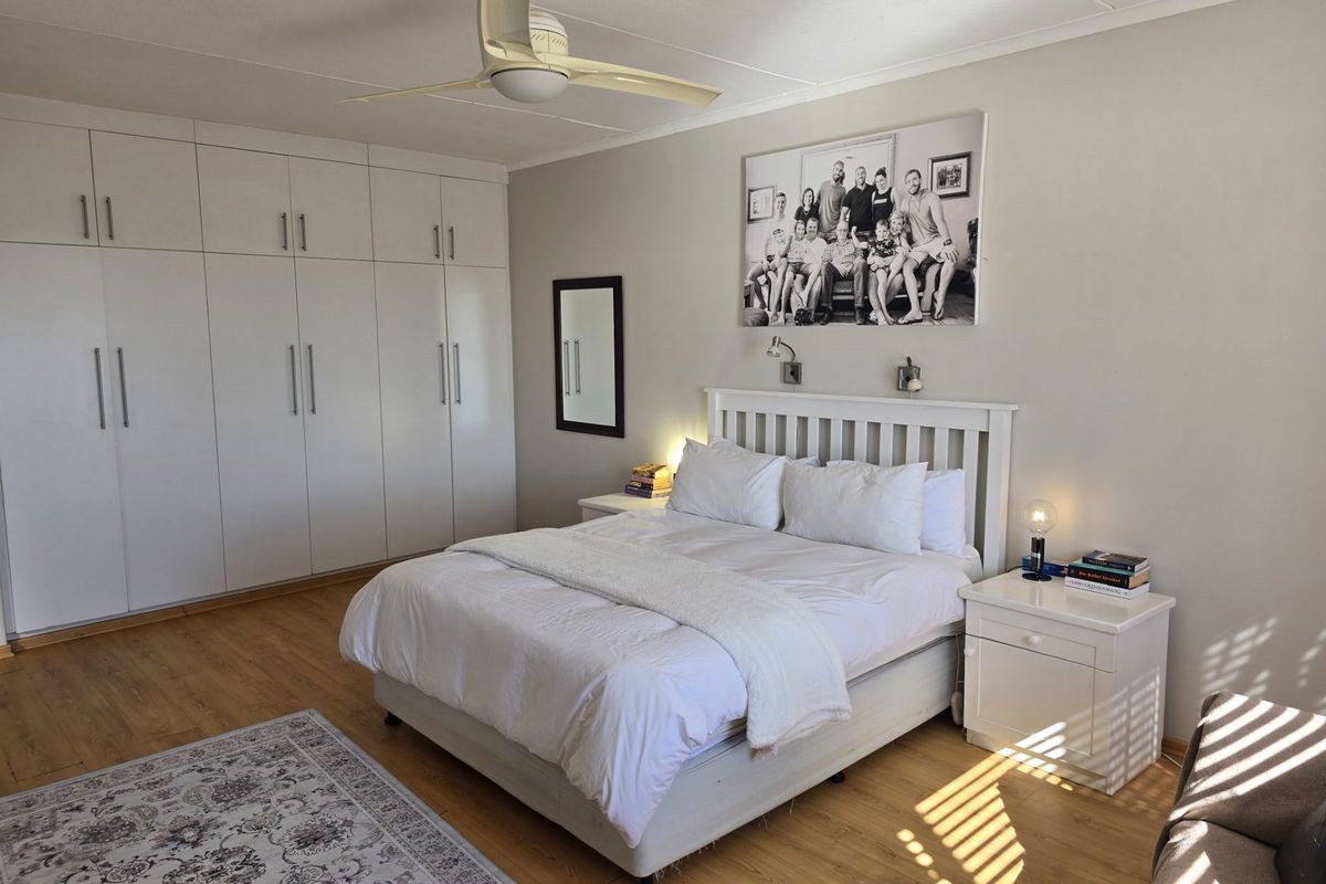 A well-maintained bedroom featuring laminate flooring, a ceiling fan, and extensive built-in cupboard storage.