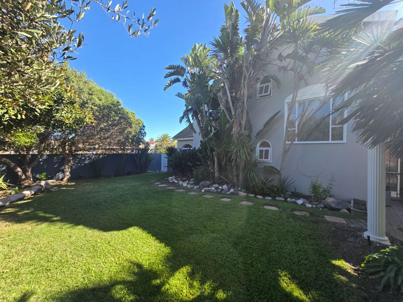 A well-maintained rear garden featuring a lush green lawn, mature landscaping, and stone garden edging alongside the exterior wall of the house.