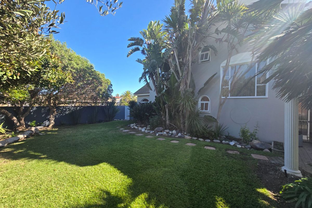A well-maintained rear garden featuring a lush green lawn, mature landscaping, and stone garden edging alongside the exterior wall of the house.