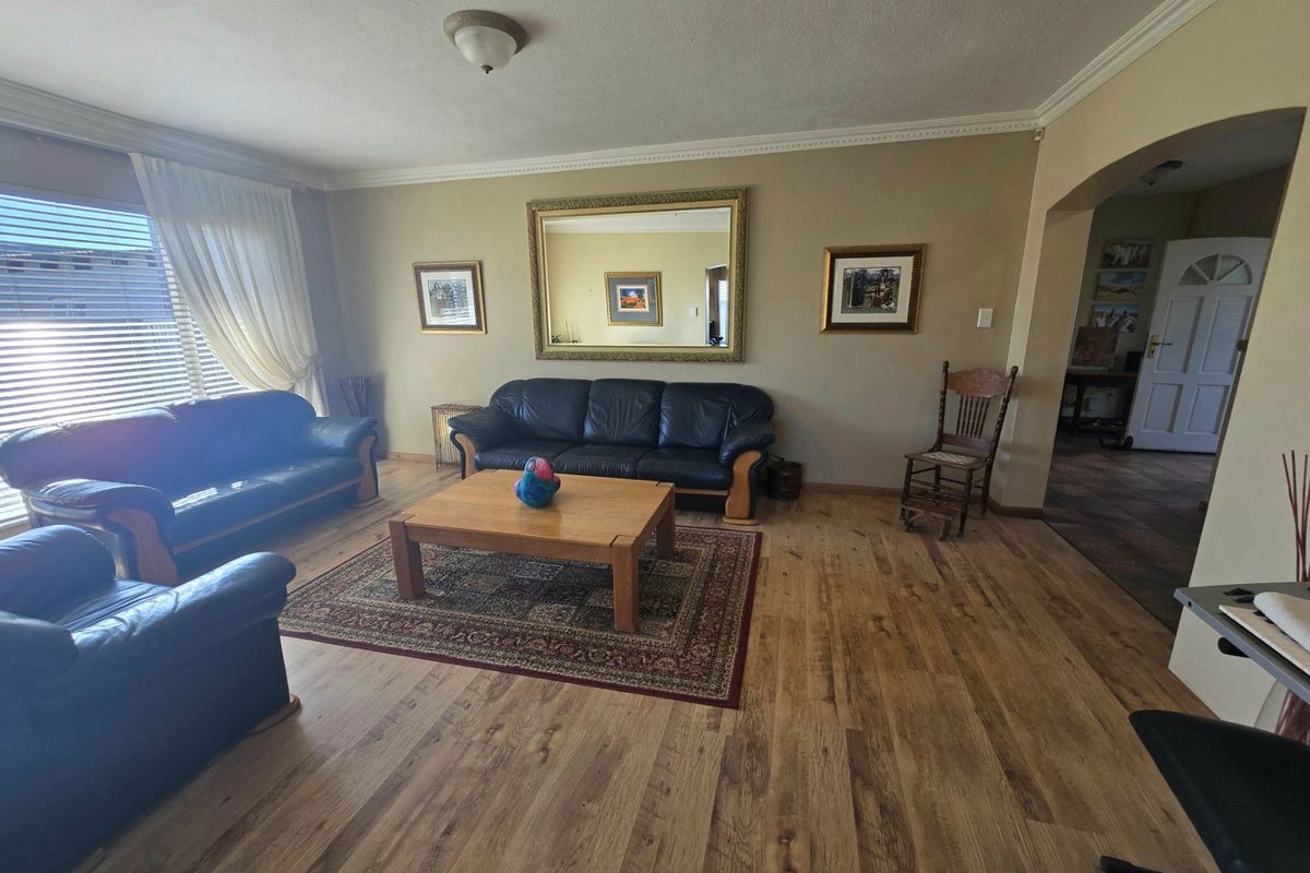 A spacious living room featuring laminate wood flooring, decorative ceiling cornicing, and an arched entryway leading to the rest of the home.