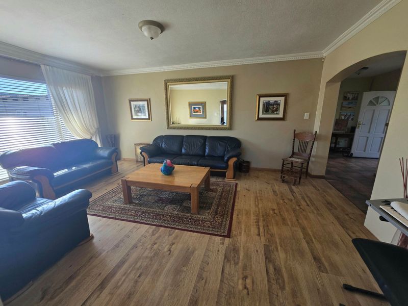 A spacious living room featuring laminate wood flooring, decorative ceiling cornicing, and an arched entryway leading to the rest of the home.