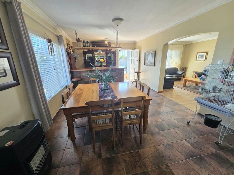 Open plan dining area featuring tiled flooring, crown molding, and a built-in bar, with an adjacent living room accessible through an archway.