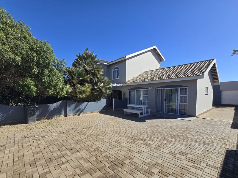 Front view of the property featuring a spacious paved driveway, tiled roof, and sliding glass door access to the main living area.