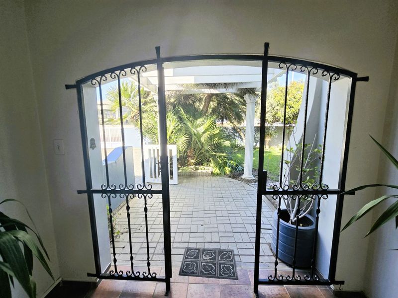 An entryway featuring a decorative wrought iron security gate opening onto a paved patio area with a pergola and garden view.