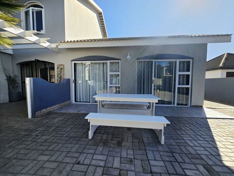 A paved outdoor patio area featuring sliding glass doors providing access to the main residence, complemented by a pergola structure.
