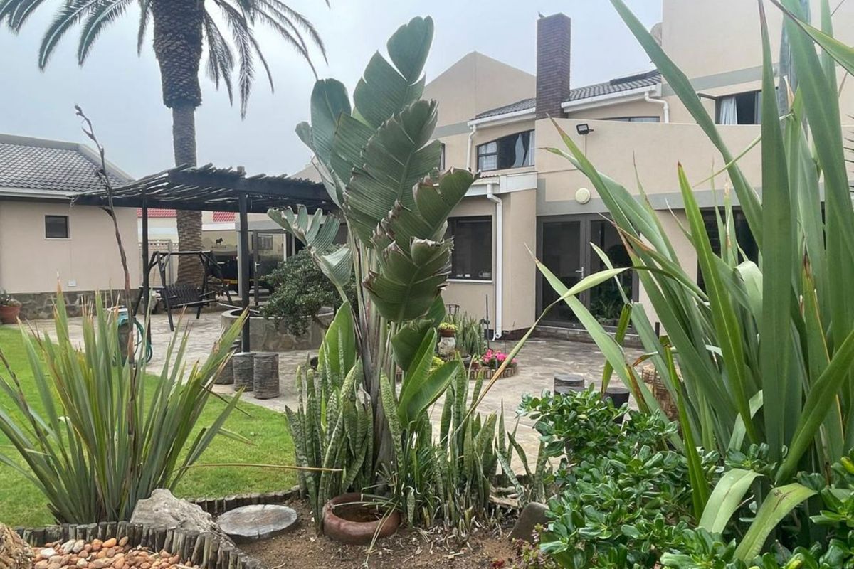 A rear exterior view of the property featuring a paved patio area, a pergola, and a landscaped garden with established plants.