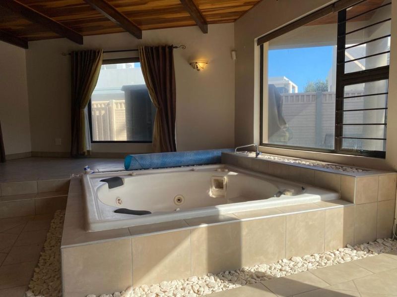 A spacious bathroom featuring a large built-in spa bath, tiled surround, and an attractive exposed timber beam ceiling with natural light.