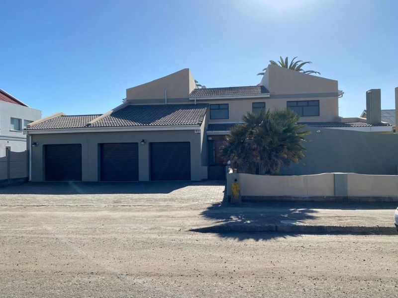 Front elevation of a multi-story residential property featuring a triple garage, tiled roof, and paved driveway access.
