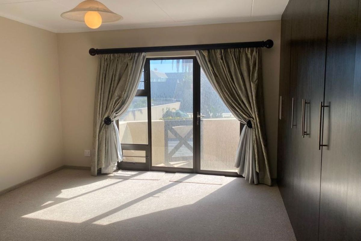 A spacious bedroom featuring built-in cupboards, neutral carpeting, and a sliding glass door providing access to an outdoor balcony area.