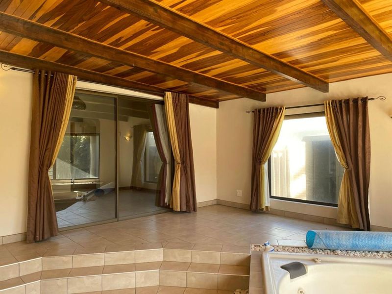 Spacious covered patio featuring a timber beam ceiling, tiled flooring, and a built-in spa bath, offering a seamless transition to the outdoors.