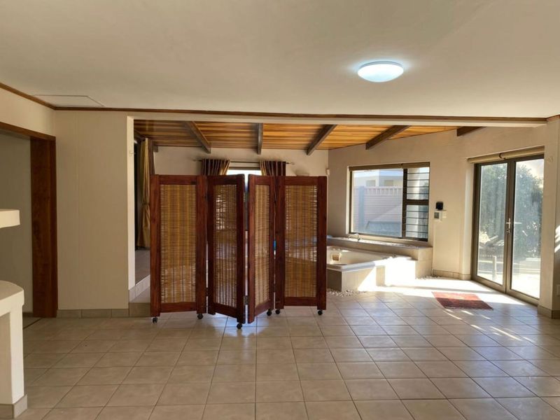 Spacious bathroom area featuring a built-in bathtub, tiled flooring, and exposed timber ceiling beams with access to the outdoors via sliding glass doors.