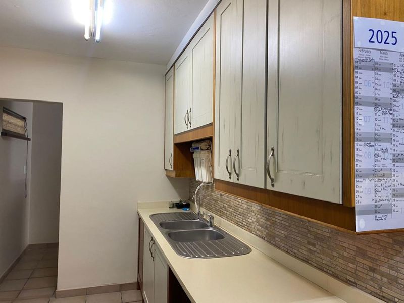 A functional scullery area featuring built-in cabinetry, a double bowl stainless steel sink, and a tiled splashback.