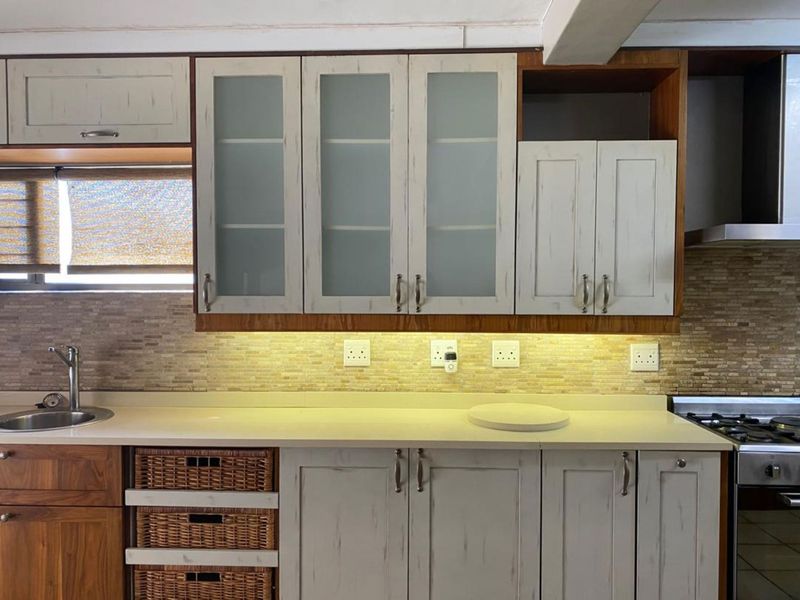 A well-maintained kitchen featuring light-toned cabinetry, stone countertops, mosaic tile backsplash, integrated hob, and extractor fan with modern under-cabinet lighting.