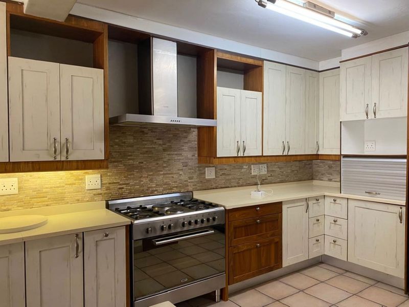 A well-maintained kitchen featuring stone countertops, a gas stove with extractor fan, tiled backsplash, and ample built-in cabinetry with an integrated appliance garage.