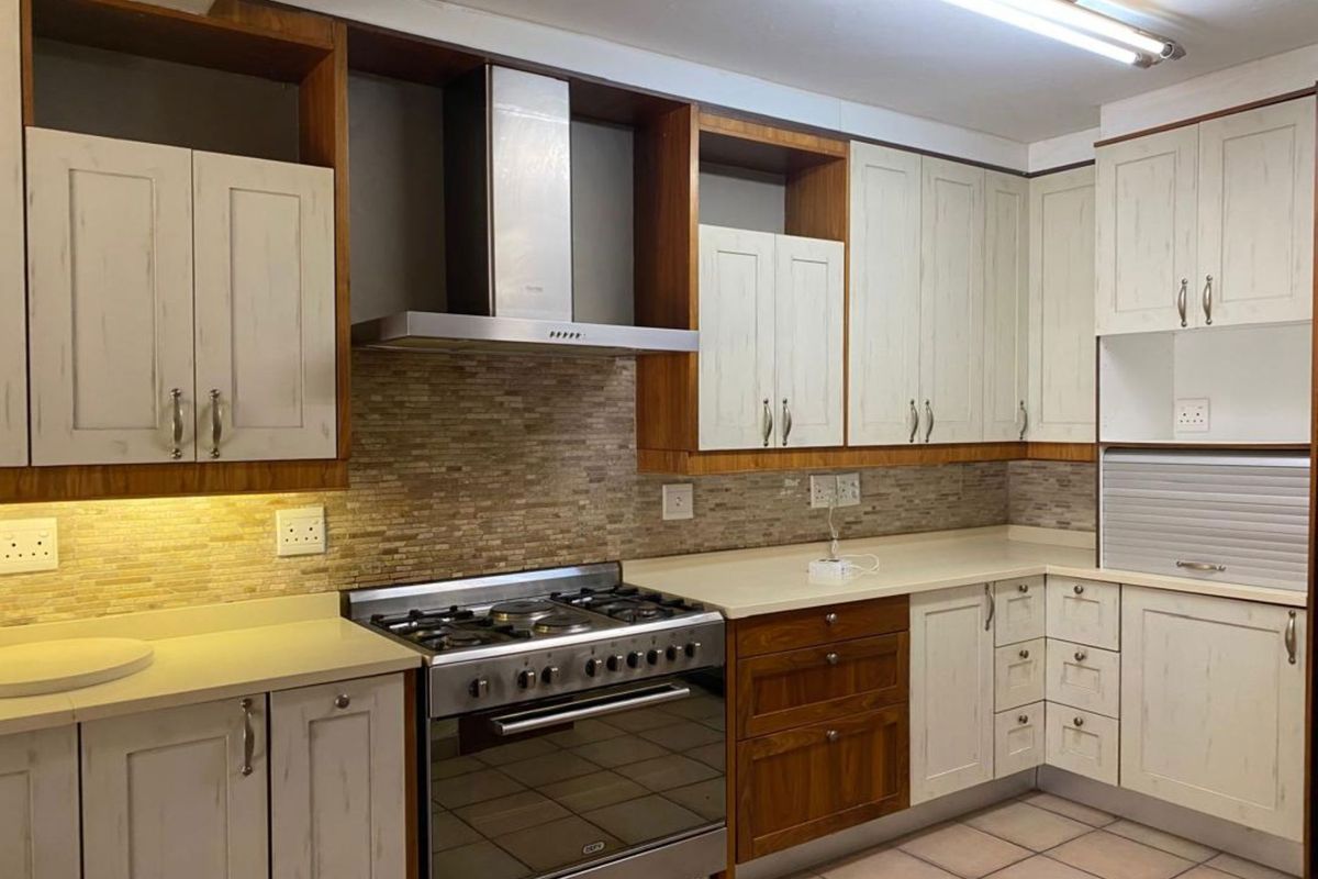 A well-maintained kitchen featuring stone countertops, a gas stove with extractor fan, tiled backsplash, and ample built-in cabinetry with an integrated appliance garage.