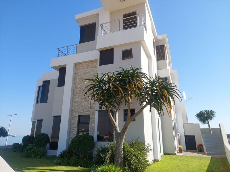 Modern multi-story residential building featuring stone cladding, tinted windows, and upper-level balconies with stainless steel railings, set within a landscaped garden.
