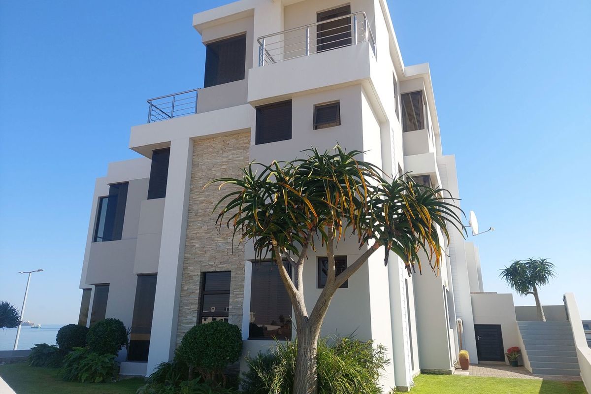 Modern multi-story residential building featuring stone cladding, tinted windows, and upper-level balconies with stainless steel railings, set within a landscaped garden.