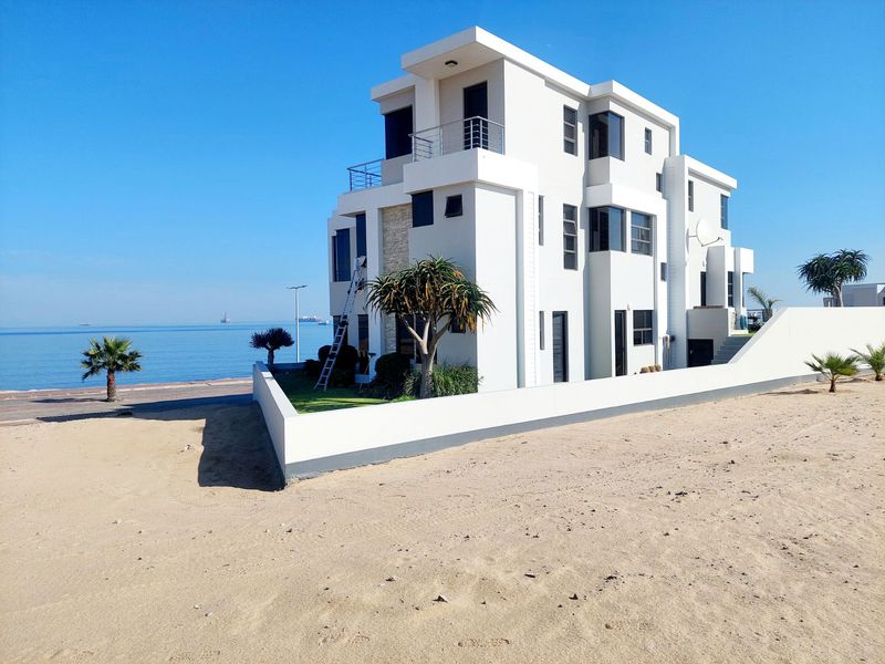 A modern multi-story beachfront house featuring clean white architectural lines, stone cladding accents, and private balconies overlooking the ocean.