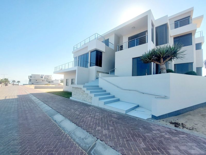 Modern multi-level architectural home featuring clean white lines, expansive glass windows, stainless steel balcony railings, and a paved entrance staircase.