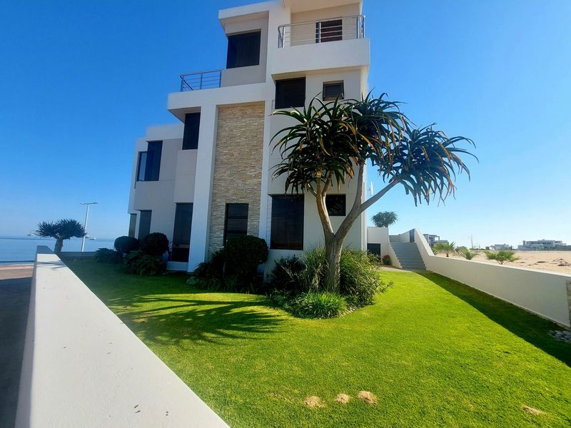 A modern multi-story coastal home featuring stone cladding, private balconies, and a well-maintained garden with a boundary wall.