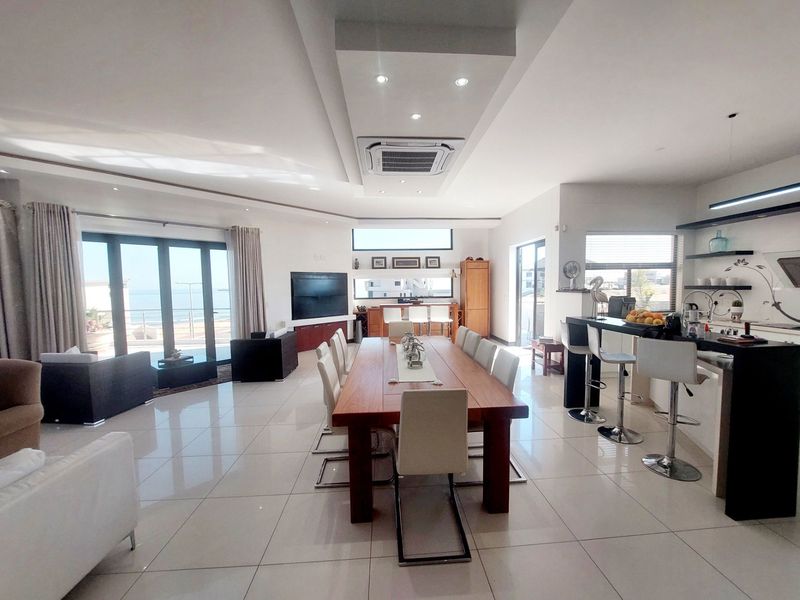 Spacious open-plan living, dining, and kitchen area featuring modern tiled floors, recessed ceiling lighting, ducted air conditioning, and seamless access to an outdoor patio.