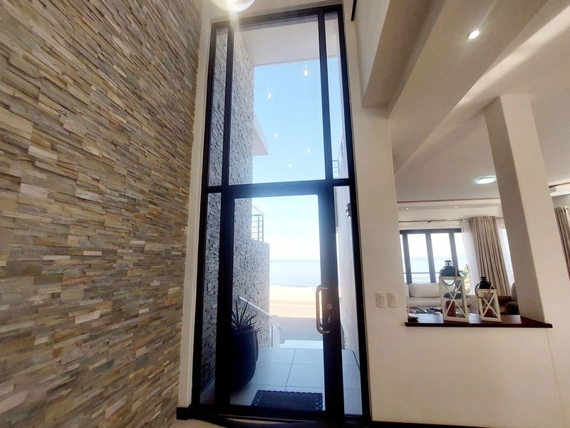 A modern, double-volume entrance featuring a striking stacked stone wall, full-height glass door, and direct views toward the beach.
