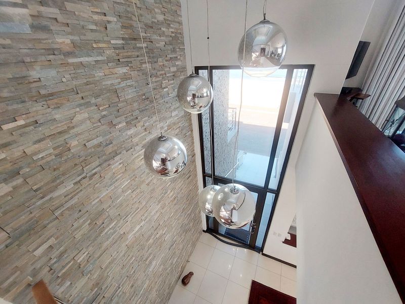 A bright, double-volume entrance hall featuring a striking stacked stone feature wall, large glass entrance door, and modern spherical pendant lighting.