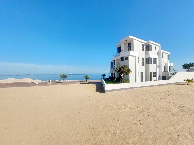 A modern multi-story beachfront house featuring clean architectural lines, multiple balconies, and direct access to the sandy coastline.